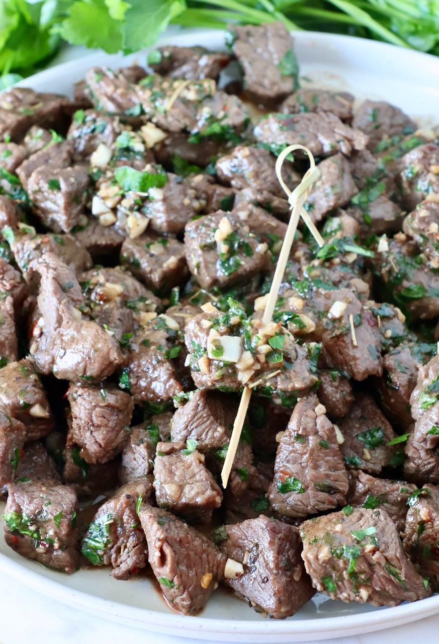 steak bites on a plate with one bite skewered on a wooden pick