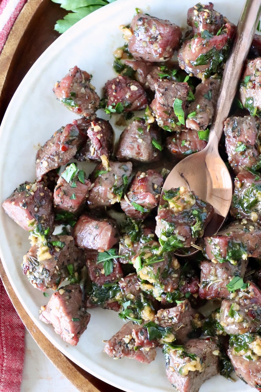 steak bites covered in garlic herb butter on a plate with a spoon