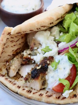 pita bread filled with chicken gyros meat, tzatziki sauce, shredded lettuce, sliced onions and tomatoes, on a plate