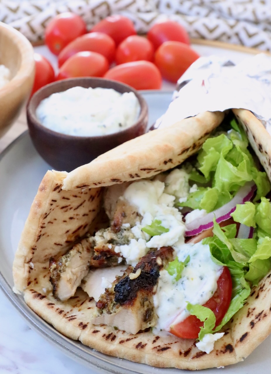 pita bread filled with chicken gyros meat, tzatziki sauce, shredded lettuce, sliced onions and tomatoes, on a plate