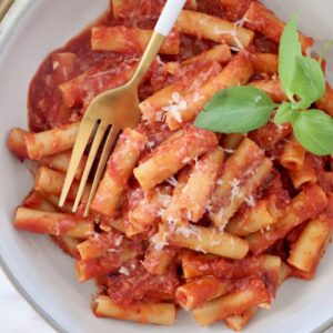 cooked ziti tossed with tomato sauce in a bowl with fresh basil leaves and a fork