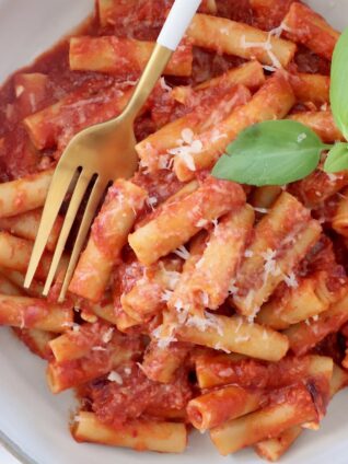 cooked ziti tossed with tomato sauce in a bowl with fresh basil leaves and a fork