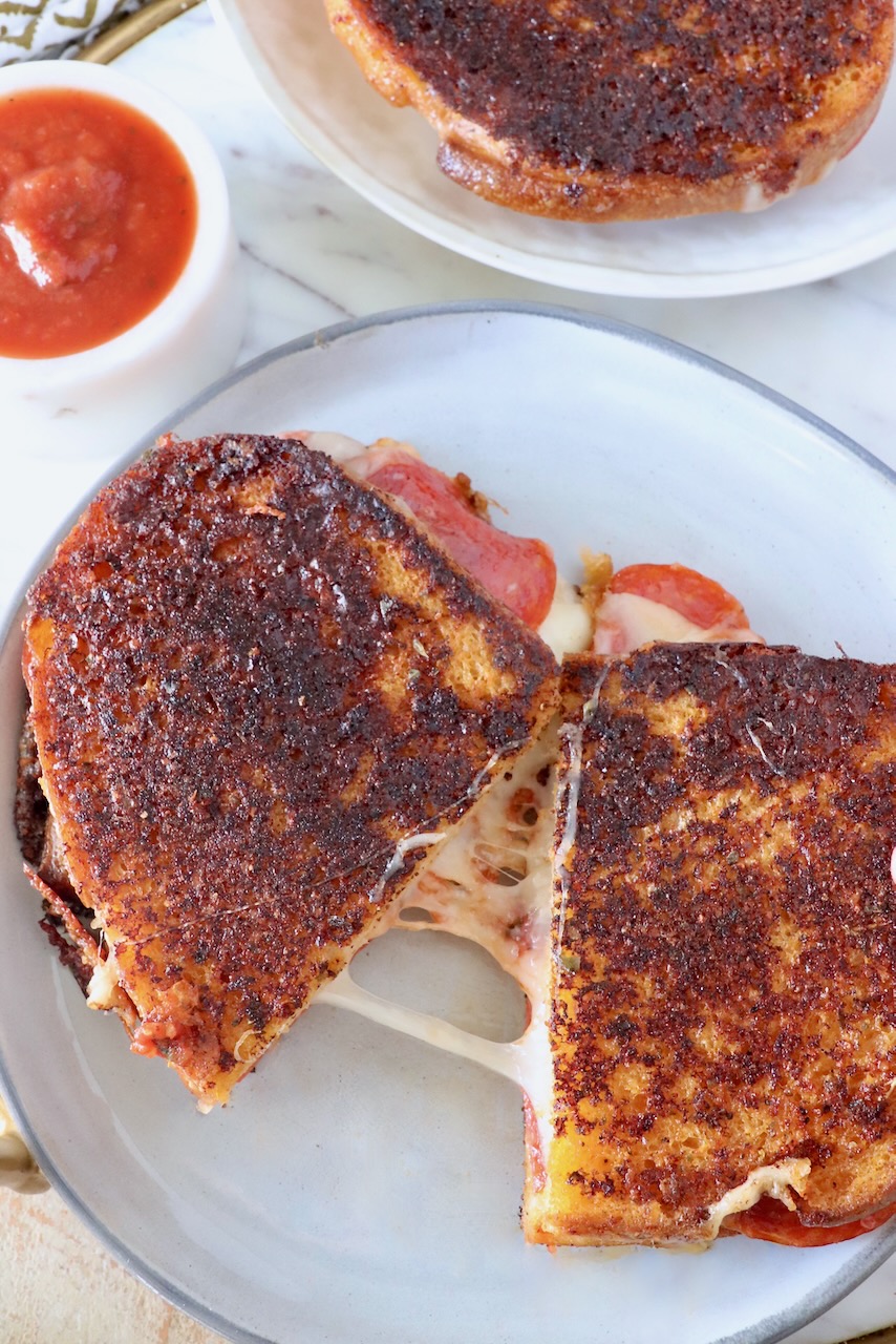 pizza grilled cheese sandwich cut in half and pulled apart on a plate next to a small bowl of pizza sauce