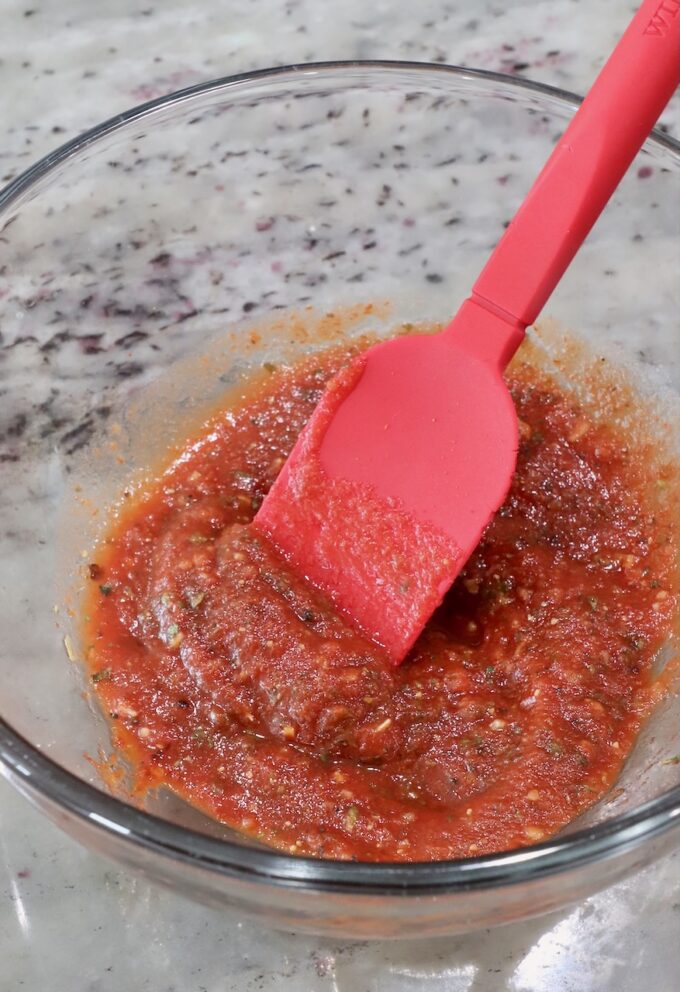 seasoned pizza sauce in a glass bowl with a red spatula