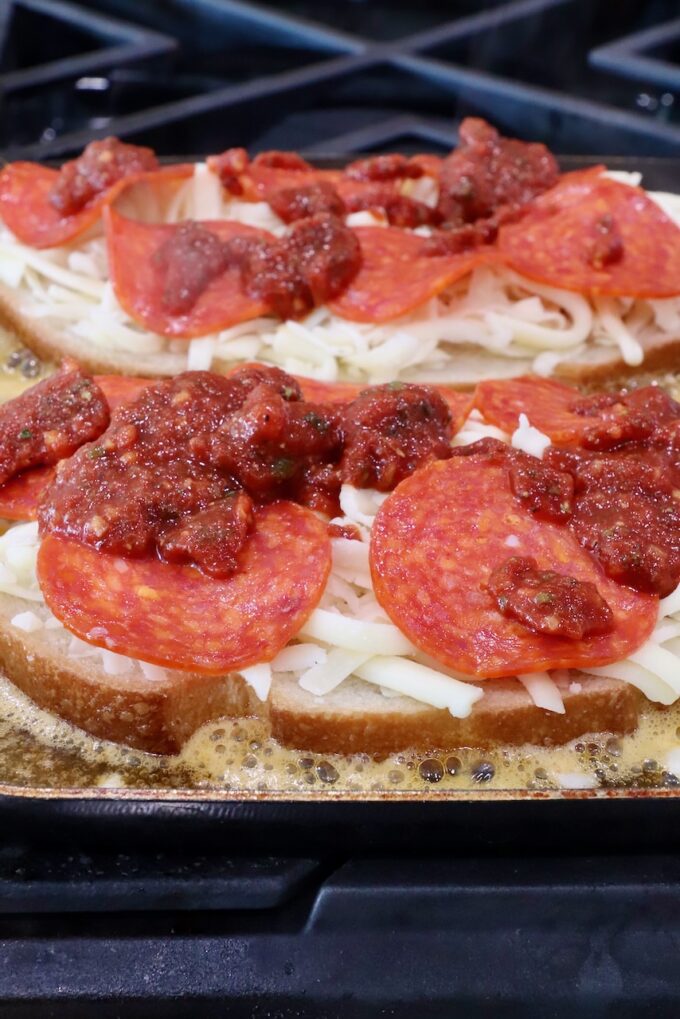 sliced bread on a skillet topped with cheese, pepperonis and pizza sauce