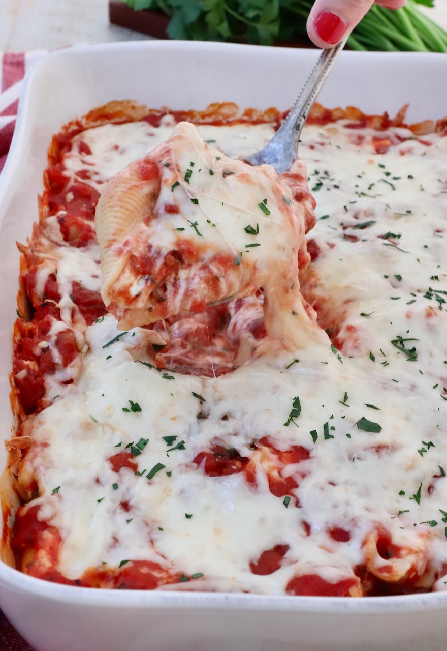 cheese filled stuffed pasta shell lifted out of a casserole dish with a serving spoon