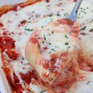 stuffed pasta shell filled with cheese and marinara sauce lifted out of a casserole dish with a serving spoon