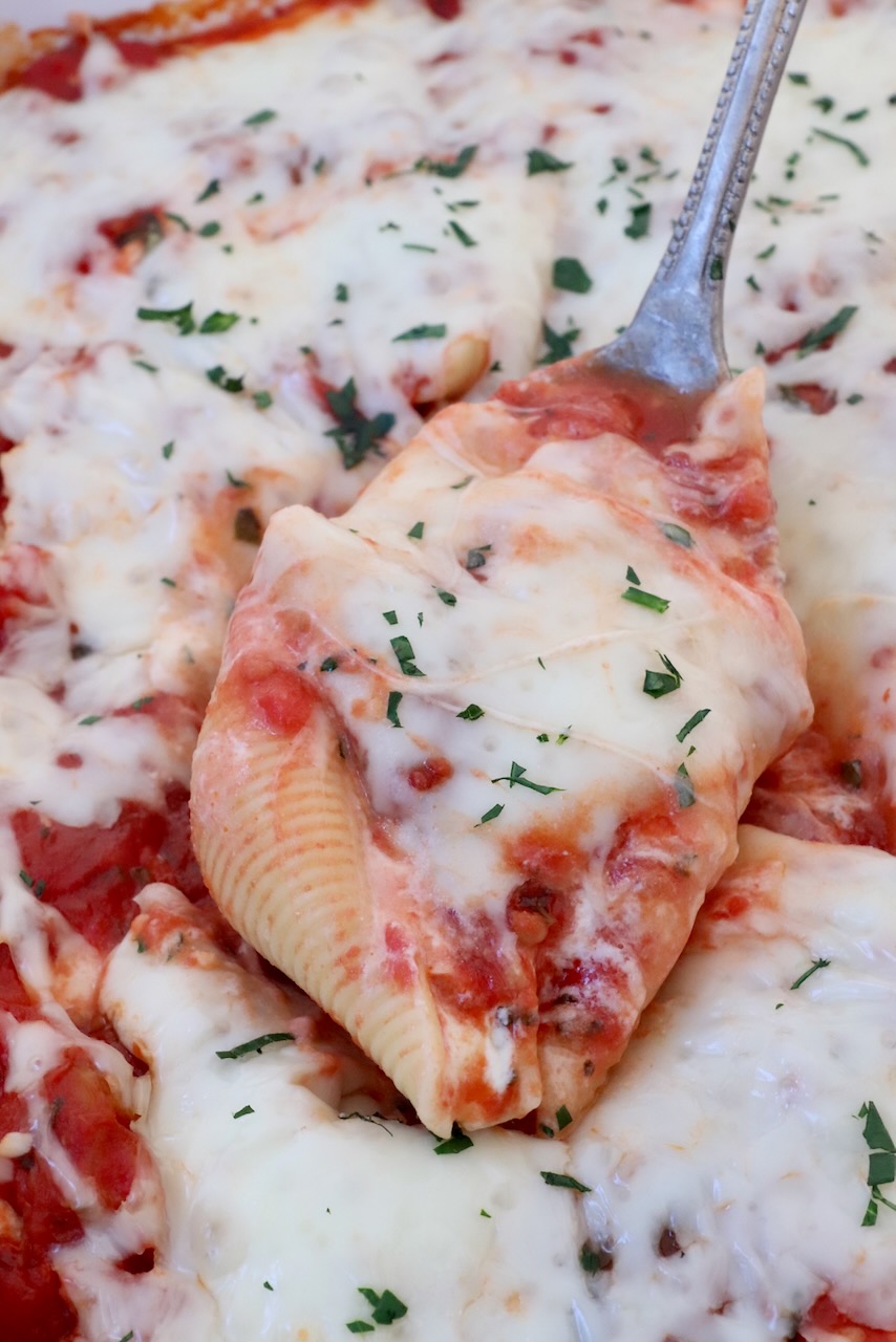 stuffed pasta shell filled with cheese and marinara sauce lifted out of a casserole dish with a serving spoon