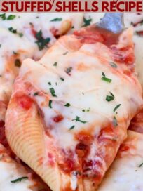 baked cheese stuffed pasta shell lifted out of a casserole dish full of stuffed shells with a large spoon