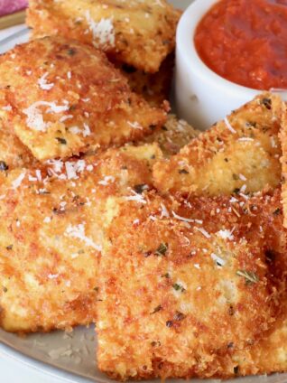 toasted raviolis stacked up on a plate with a small bowl of marinara sauce on the plate