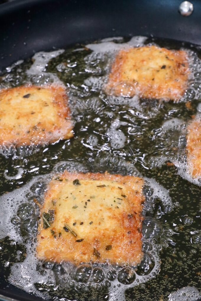 breadcrumb coated raviolis cooking in a skillet of oil