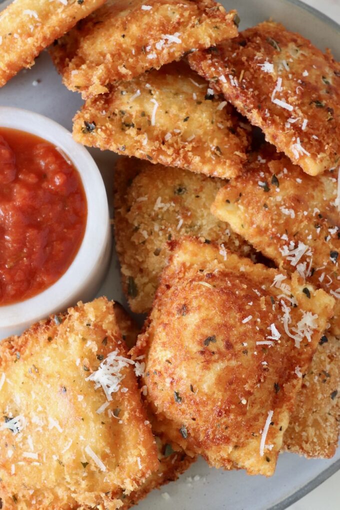 toasted raviolis stacked up on a plate with a small bowl of marinara sauce on the side