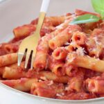 cooked ziti pasta tossed in tomato sauce in a bowl with a fork