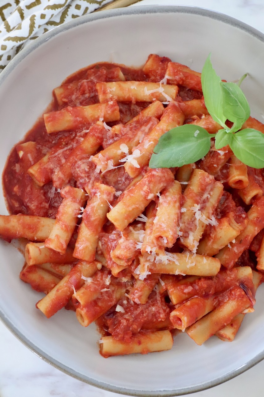 cooked pasta tossed with tomato nduja sauce in a bowl with fresh basil leaves