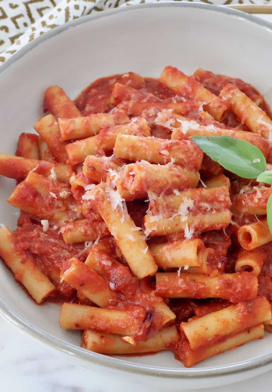 ziti pasta tossed with tomato sauce in a bowl with fresh basil leaves