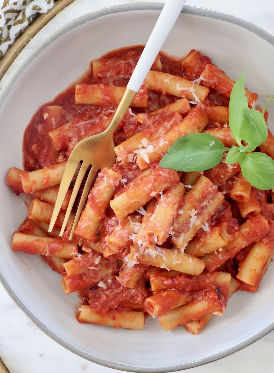 cooked ziti tossed with tomato sauce in a bowl with fresh basil leaves and a fork