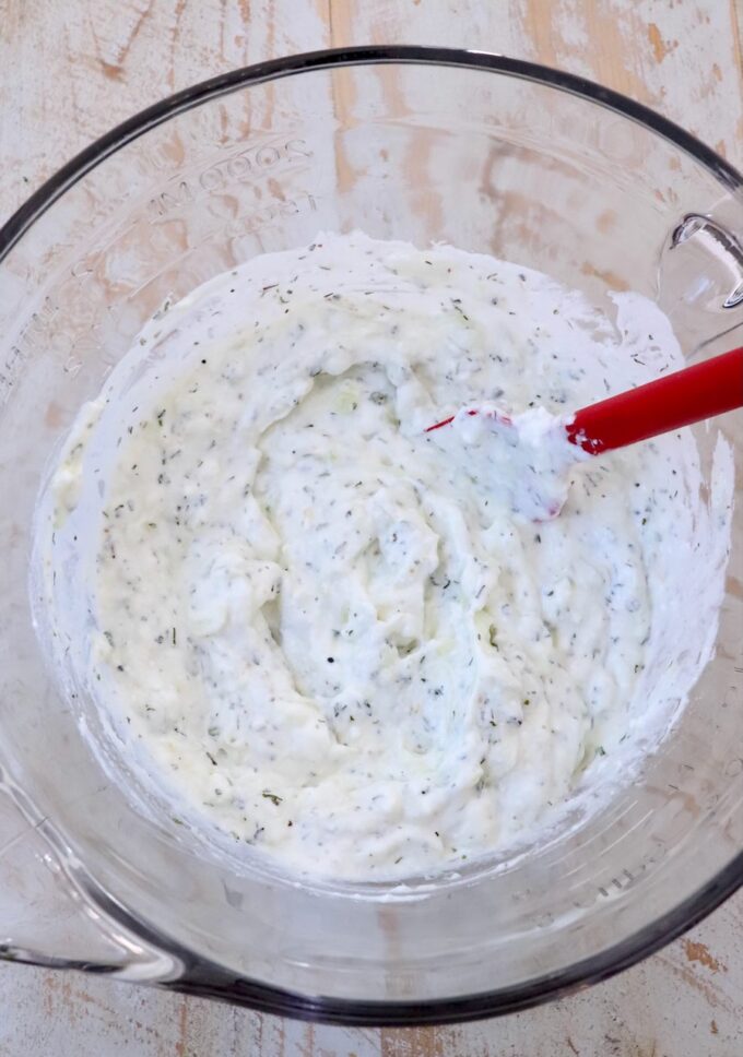 tzatziki sauce mixed up in a large glass bowl with a red spatula