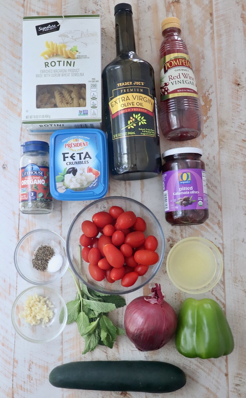 ingredients for Greek pasta salad on a white wood board