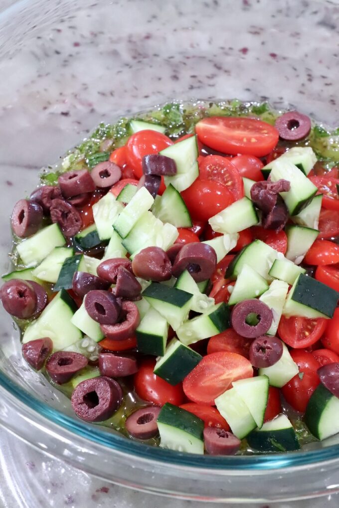 diced cucumber, tomatoes and olives in a large glass bowl