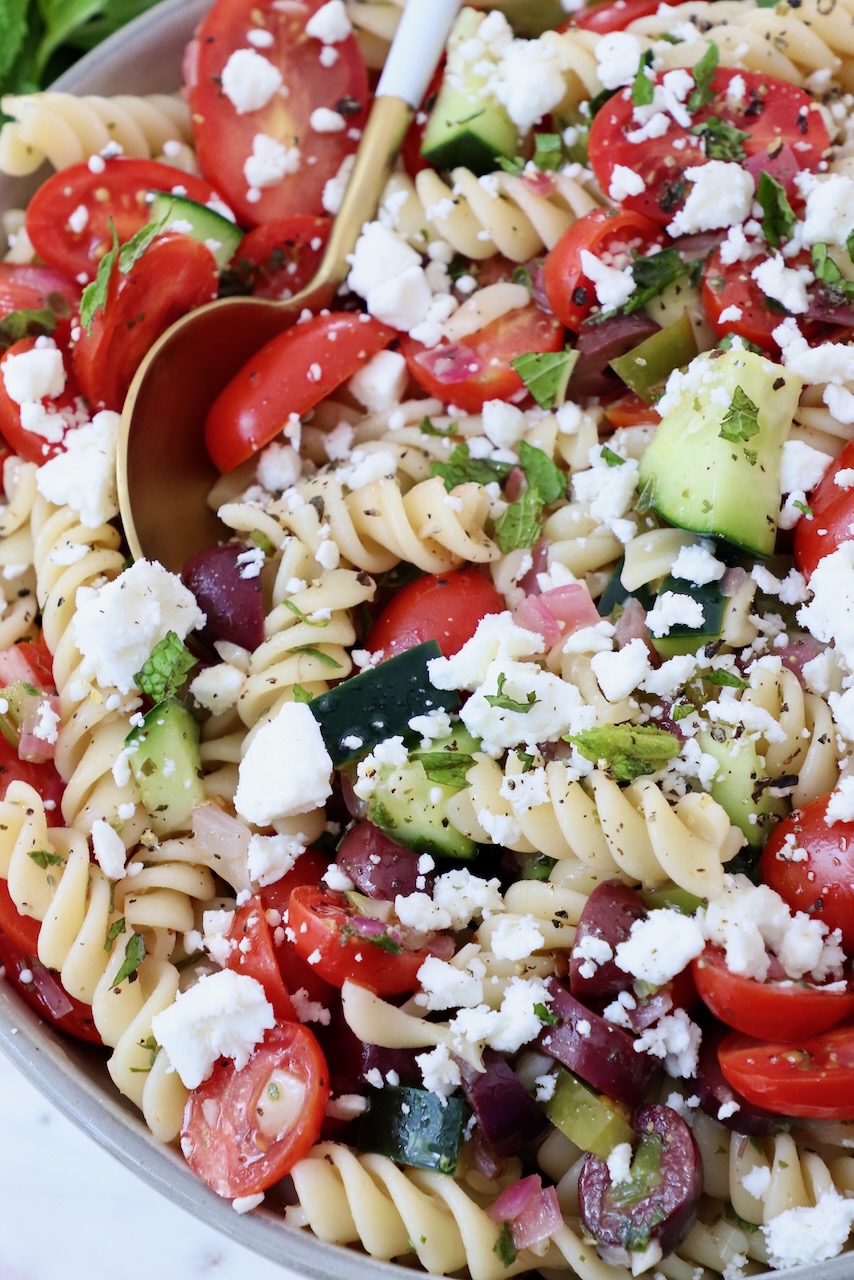 pasta salad topped with crumbled feta cheese in a bowl with a spoon