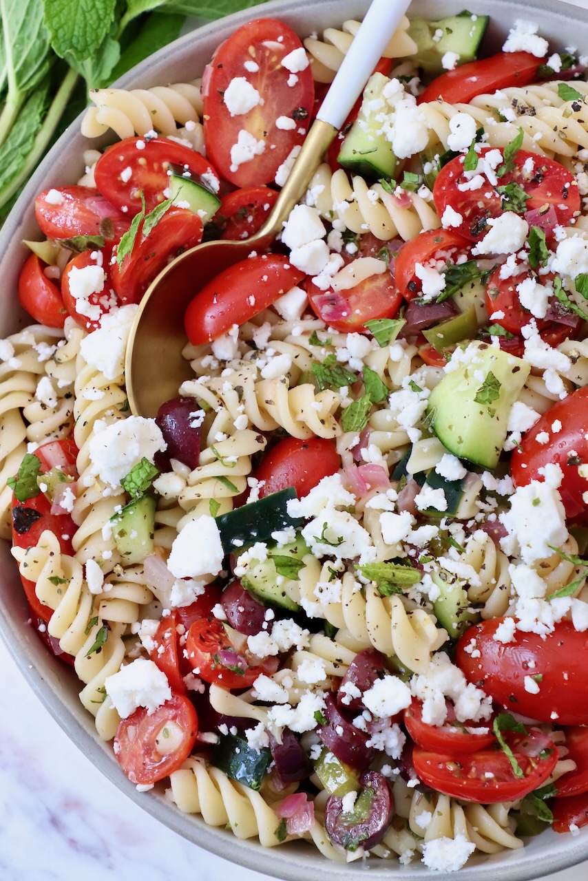 pasta salad with cucumber and tomatoes in a bowl with a spoon