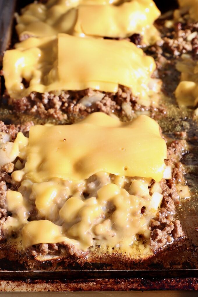 ground beef topped with slices of American cheese on a griddle