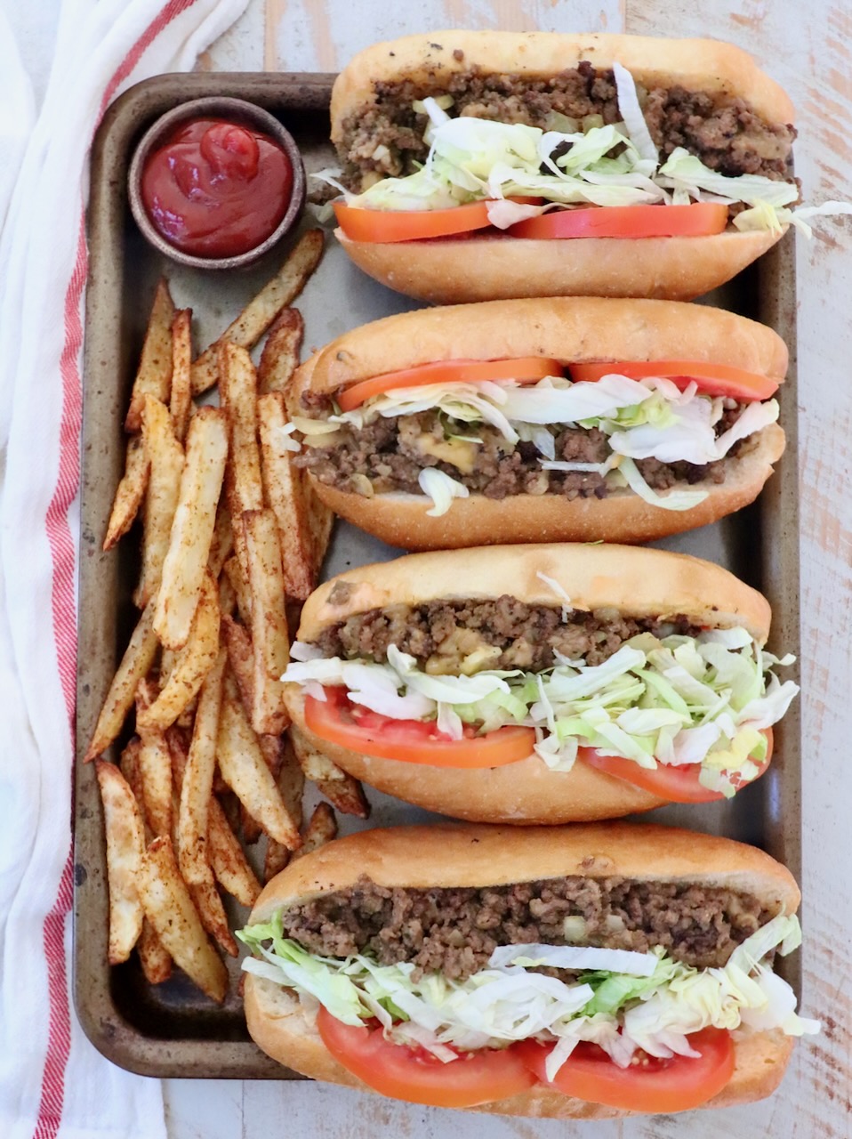 four chopped cheese sandwiches on a baking sheet with cooked fresh fries and a small bowl of ketchup