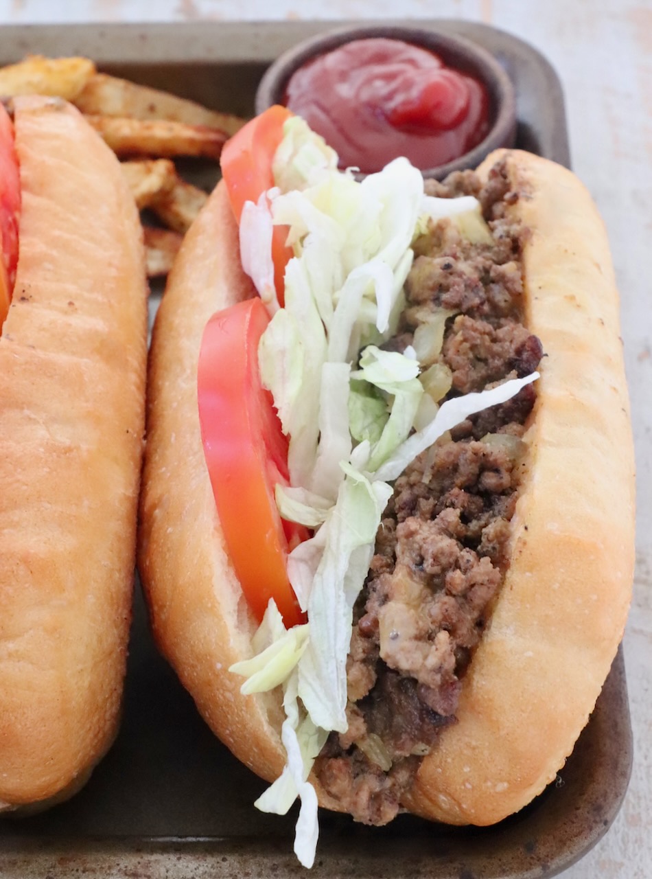 chopped cheese sandwich on a metal baking sheet with a small bowl of ketchup behind the sandwich