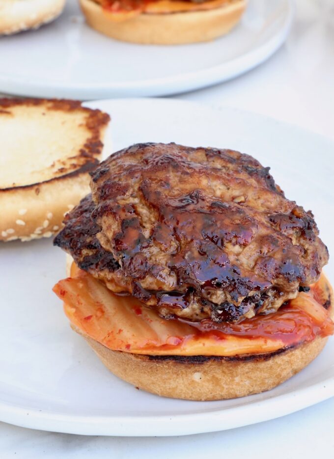 hamburger bun on a plate topped with kimchi and bbq glazed burger patties