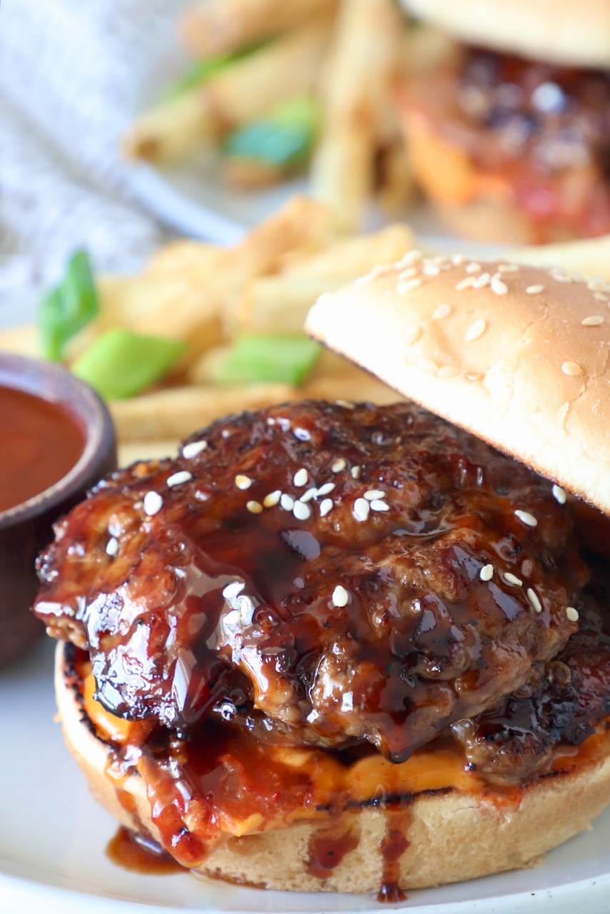 korean bbq burger on a bun on a plate, with the top bun leaning on the side of the burger