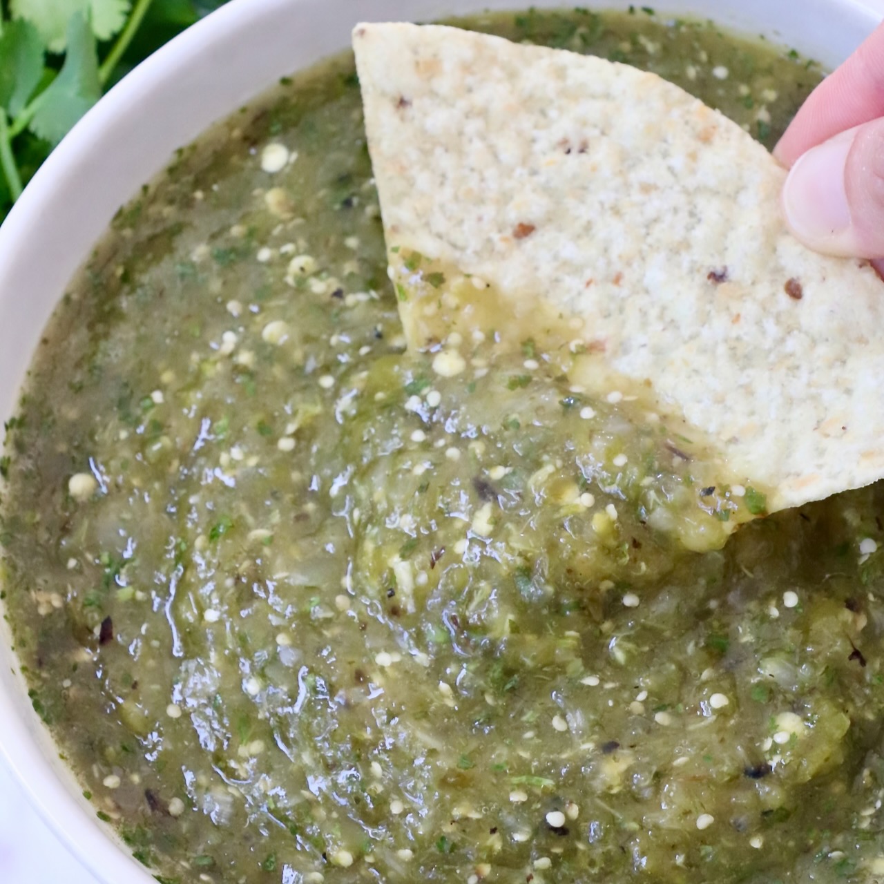 tomatillo salsa in a bowl with a hand dipping a tortilla chip in the salsa