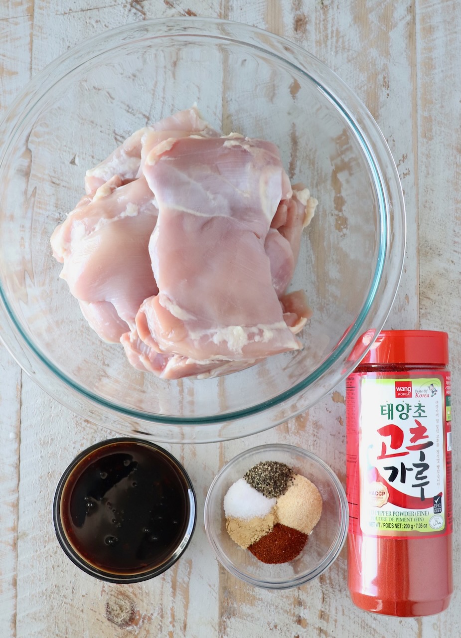 ingredients for korean bbq chicken in glass bowls on a white wood board