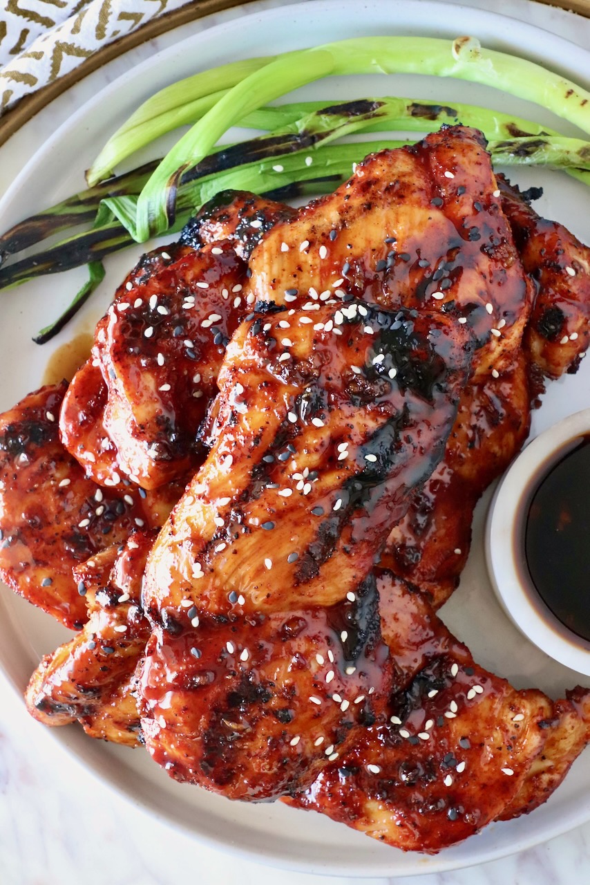 grilled chicken covered in bbq sauce stacked up on a plate with green onions on the side