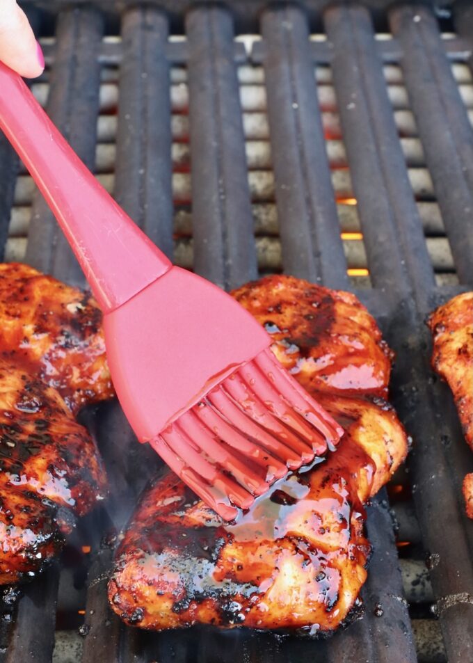 red brush with bbq sauce brushed on a grilled chicken thigh on a grill
