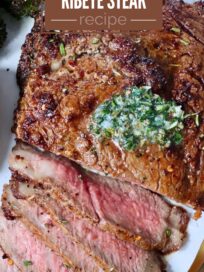 partially sliced cooked ribeye steak on a plate with herb butter on top