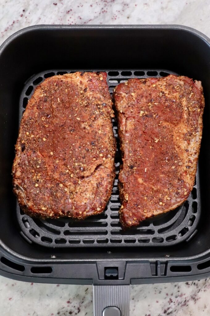 seasoned ribeye steaks in an air fryer basket