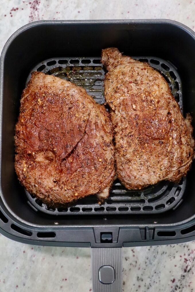 seasoned ribeye steaks in an air fryer basket