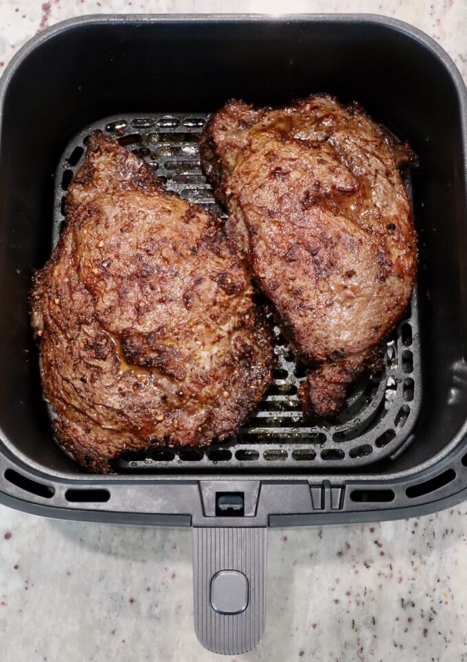 cooked ribeye steaks in an air fryer basket