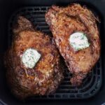 cooked ribeye steaks in an air fryer basket topped with herb compound butter