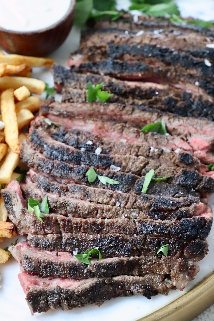 sliced steak on a platter with french fries and a small bowl of sauce on the side