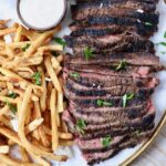 sliced steak on a platter next to french fries and a small bowl of sauce