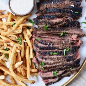 sliced steak on a platter next to french fries and a small bowl of sauce