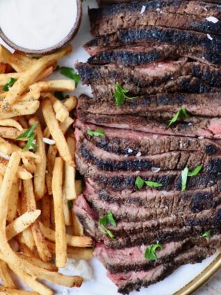sliced steak on a platter next to french fries and a small bowl of sauce