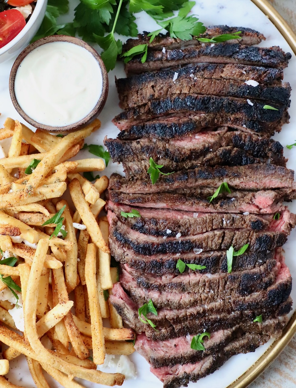 sliced steak on a platter with french fries and a small bowl of sauce
