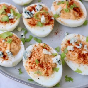 buffalo deviled eggs on a plate with a sprinkle of blue cheese crumbles and chopped green onions on top