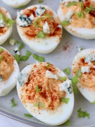 buffalo deviled eggs on a plate with a sprinkle of blue cheese crumbles and chopped green onions on top