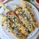 grilled corn on the cob on a plate topped with blue cheese crumbles and fresh chopped cilantro