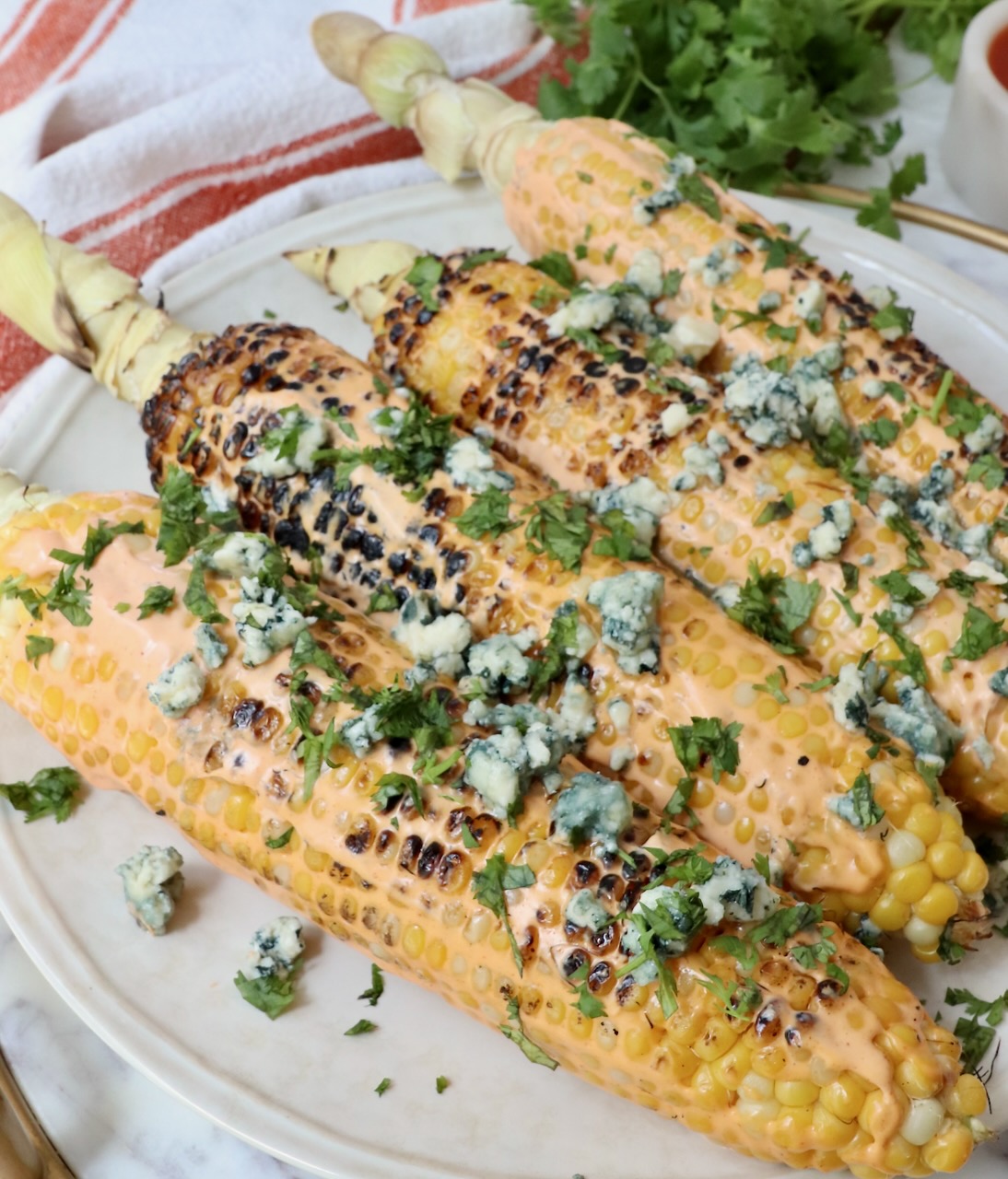 grilled corn on the cob on a plate, topped with blue cheese crumbles and chopped cilantro