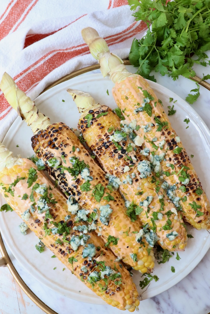 grilled corn on the cob on a plate topped with blue cheese crumbles and fresh cilantro