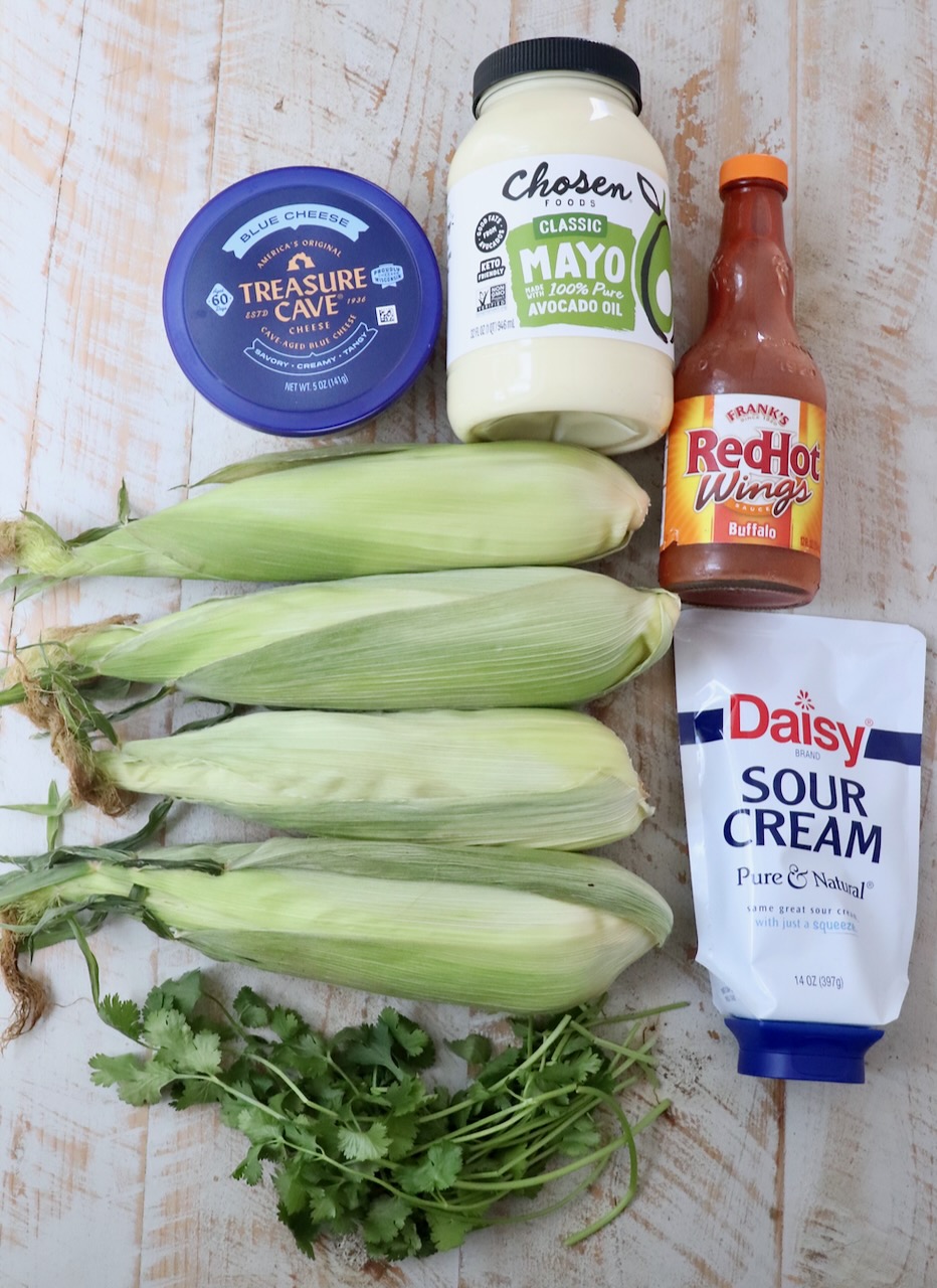 ingredients for elote with buffalo sauce on a white wood board